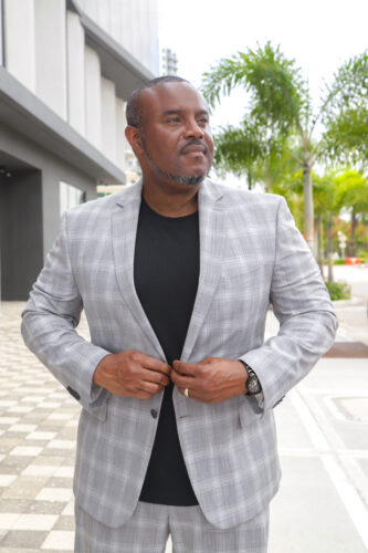 "Cornelius, a South Florida photographer, walking confidently in a tailored suit on a sunny downtown city walk, embodying professionalism and style."